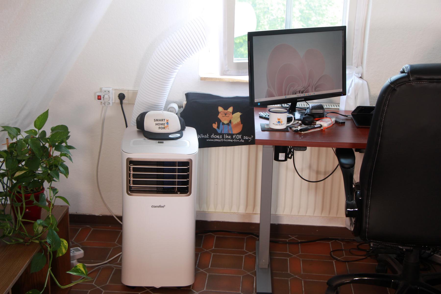 Eine mobile Klimaanlage steht im Test auf einem Tisch und der Abluftschlauch ist zum Fenster herausgelegt.